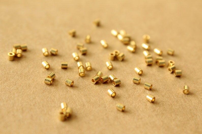 May include: A close-up of a group of gold jump rings scattered on a brown surface. The jump rings are small and round, with a hole in the center. They are used for connecting jewelry pieces together.