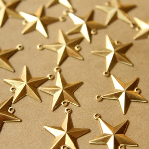 May include: A collection of gold-toned metal star-shaped charms with a five-pointed design. The charms have two small loops at the top for attaching to jewellery or other crafts.