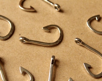 May include: A close-up of nine silver-colored fishing hooks on a brown surface.