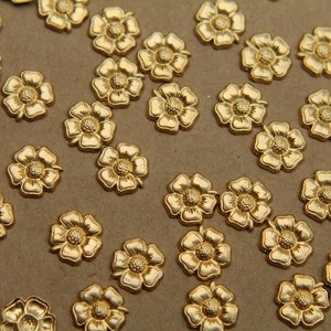May include: A collection of gold-colored metal flower-shaped embellishments. The flowers have five petals and a raised center.
