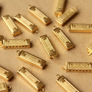 May include: A collection of gold-coloured harmonicas with a musical note design. Each harmonica has a small loop at the top for hanging.