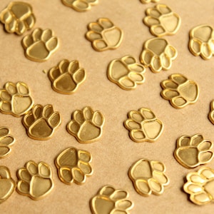 May include: A collection of gold-coloured metal paw prints, scattered on a brown surface.