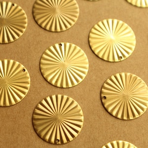 May include: A collection of gold-colored metal round embellishments with a sunburst design. The embellishments have a hole in the center and are arranged in a grid pattern on a brown surface.