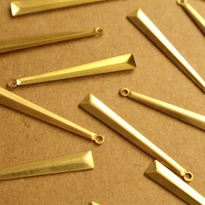 Könnte beinhalten: Eine Sammlung goldfarbener Metall-Anhänger mit einer spitzen, dreieckigen Form. Die Anhänger haben oben ein Loch zum Anbringen an Schmuck.