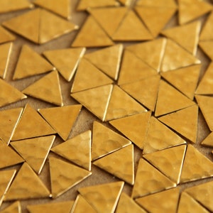 May include: A close-up of a surface covered in small, gold-colored, triangular metal pieces. The pieces are arranged in a random pattern, creating a textured and shimmering effect.