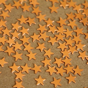 May include: A close-up image of a brown surface covered with numerous small, copper-colored star-shaped embellishments.