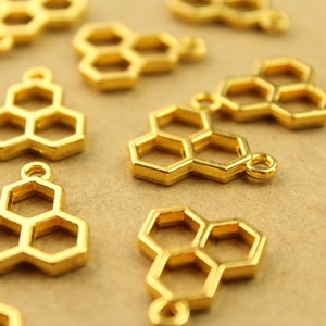 May include: A group of gold-colored metal charms shaped like honeycombs. The charms have a loop at the top for attaching to jewelry or other crafts.