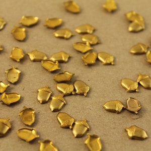 May include: A scattering of gold-colored acorn-shaped metal charms on a brown surface.