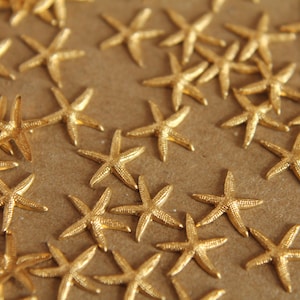 May include: A close-up of a large quantity of gold-colored starfish scattered on a brown surface. The starfish are all the same size and shape, and they are arranged in a random pattern.