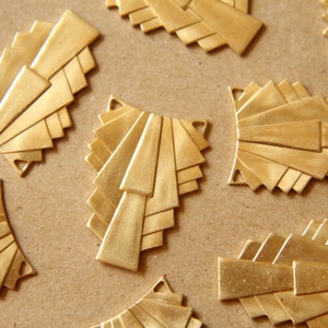 May include: A group of eight gold-colored metal decorative pieces with a geometric fan design. The pieces are arranged on a brown surface.