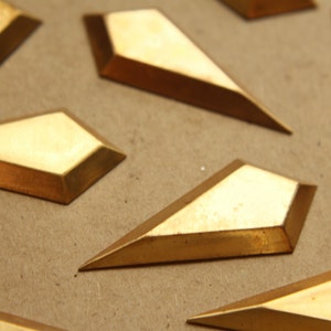 Könnte beinhalten: Nahaufnahme von mehreren goldfarbenen, geometrischen, rautenförmigen Metallteilen auf einer braunen Oberfläche.