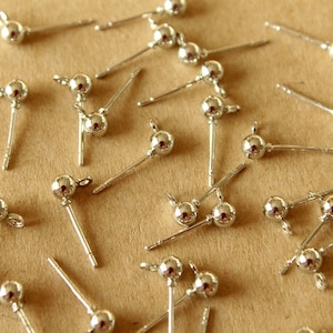 May include: A close-up of a group of silver earring findings with a small ball at the top. The findings are scattered on a brown surface.