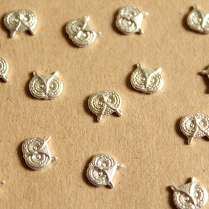 May include: A collection of silver owl charms, each with a detailed design. The charms are arranged on a brown surface.