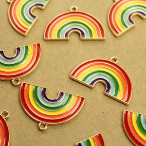 Könnte beinhalten: Eine Sammlung goldfarbener Regenbogen-Anhänger mit farbenfroher Emaille-Oberfläche. Die Anhänger sind halbkreisförmig und als volle Bögen geformt und haben oben eine Öse zum Anbringen an Schmuck oder andere Bastelarbeiten.