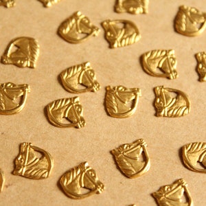 May include: A collection of gold-toned metal horse head charms. The charms are scattered on a brown surface.
