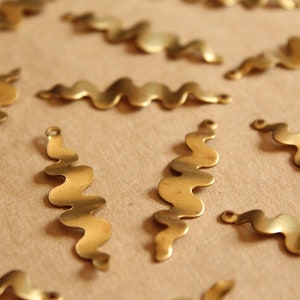 K&ouml;nnte beinhalten: Eine Sammlung von wellenf&ouml;rmigen Metallformen in Gold, jede mit einem leicht anderen Design. Die Formen sind auf einer braunen Oberfl&auml;che angeordnet.