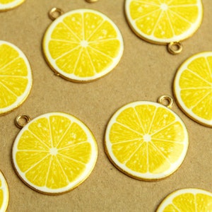 May include: A collection of gold-toned metal charms shaped like lemon slices. Each charm features a yellow lemon slice with a white center and a detailed texture.