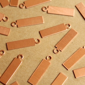 May include: A collection of copper-coloured metal tags with a hole at the top. The tags are rectangular and have a smooth, slightly textured surface.