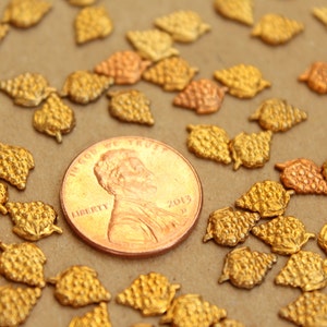 May include: A close-up of a group of gold-colored metal grape clusters. The clusters are scattered on a brown surface, with a US penny in the center for scale.
