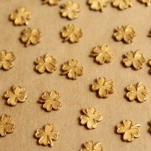 May include: A collection of gold-colored four-leaf clover charms scattered on a brown surface.