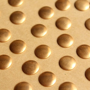 May include: A close-up of a sheet of brown paper with a pattern of evenly spaced, round, gold-colored metal tacks.