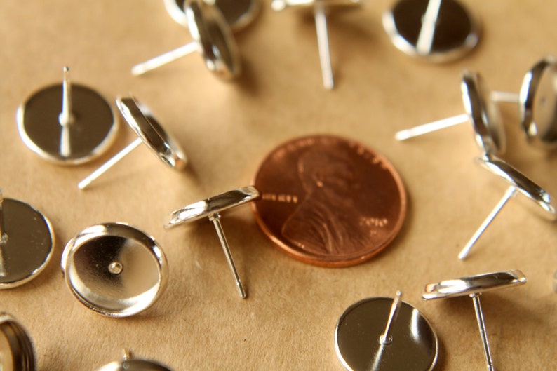 May include: A close-up of a group of silver earring posts with round backs. The earring posts are arranged in a circle around a penny.