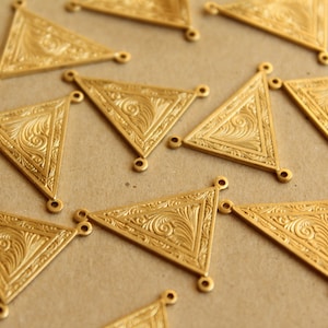 Peut inclure: Gros plan de plusieurs breloques triangulaires dorées avec des motifs tourbillonnants ornés. Chaque breloque comporte trois petites boucles pour l'attache à d'autres composants. Les breloques sont probablement destinées à la fabrication de bijoux ou à d'autres projets artisanaux.