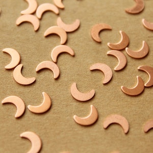 Może przedstawiać: Kolekcja miedzianych kształtów półksiężyca rozrzuconych na brązowej powierzchni.