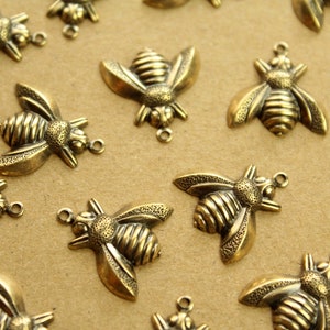May include: A collection of gold-toned metal bee charms with intricate details. The bees have a textured surface and are perfect for adding a touch of whimsy to jewelry or crafts.
