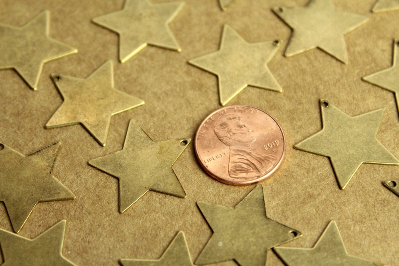 Peut inclure: Gros plan sur une collection de breloques en forme d'&eacute;toile en laiton, &eacute;parpill&eacute;es sur une surface brune. Une pi&egrave;ce de monnaie de cuivre de 1 centime est au centre de l'image.
