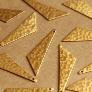 May include: A collection of gold-toned metal triangle shapes with a hammered texture. The triangles are scattered on a brown surface.