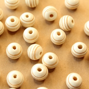 May include: A collection of white wooden beads with brown stripes. The beads are round and have a hole in the center. They are arranged in a random pattern on a light brown surface.