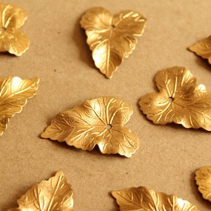 May include: Ten gold-colored metal leaf-shaped embellishments with a hole in the center of each leaf. The leaves are arranged on a brown surface.