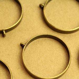 May include: Five gold-colored metal hoops with a small loop on one side. The hoops are arranged on a brown surface.