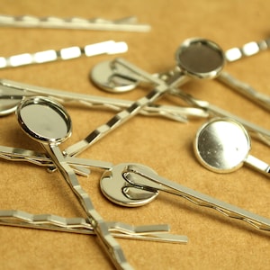 Op de afbeelding: Een groep zilveren haarclips met ronde, zilverkleurige, platte versieringen.