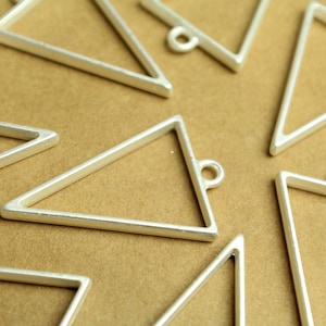 May include: A group of silver triangle-shaped metal frames with a loop at the top. The frames are arranged on a brown surface.