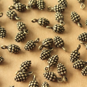 May include: A collection of antique gold-toned metal pine cone charms. The charms are detailed with a textured surface and have a loop for attaching to jewellery or other crafts.