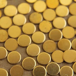 Könnte beinhalten: Nahaufnahme einer großen Menge kleiner, runder, goldfarbener Metallscheiben. Die Scheiben sind zufällig auf einer braunen Oberfläche verteilt.
