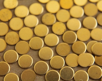 May include: A close-up of a large quantity of small, round, gold-colored metal discs. The discs are scattered randomly on a brown surface.