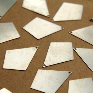 May include: A collection of silver-colored metal diamond-shaped charms with a hole in each corner. The charms are scattered on a brown surface.