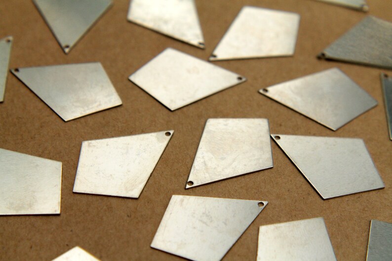 May include: A collection of silver-colored metal diamond-shaped charms with a hole in each corner. The charms are scattered on a brown surface.