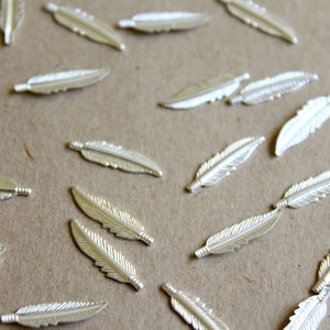May include: A collection of silver-colored metal feathers scattered on a brown surface. The feathers are all the same size and shape, and they have a slightly textured surface.