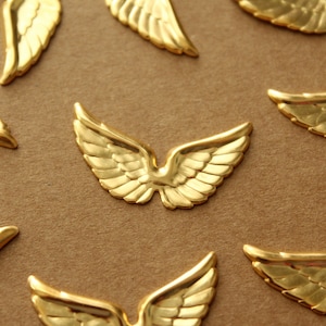 Puede incluir: Una colección de alas de ángel de metal dorado, esparcidas sobre una superficie marrón. Las alas están detalladas con intrincados patrones y tienen una textura ligeramente en relieve.