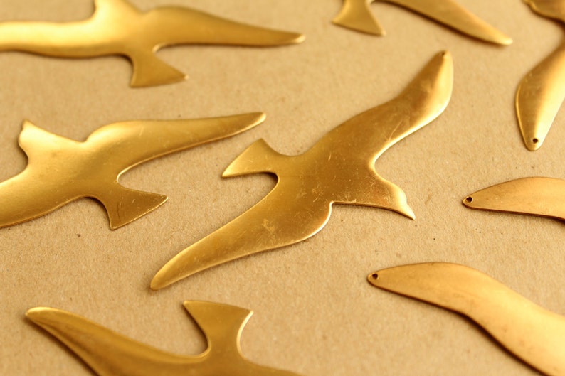 May include: A collection of seven gold-colored metal bird cutouts. The birds are in various sizes and shapes, with some having a more realistic bird shape and others being more abstract.
