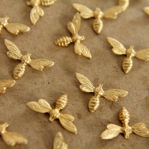 May include: A collection of gold-colored bee-shaped charms. The charms are arranged on a brown surface.