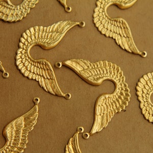 Puede incluir: Una colección de alas de ángel de metal de color dorado con una superficie texturizada. Las alas están dispuestas en un patrón aleatorio sobre un fondo marrón.