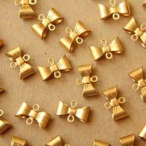 May include: A collection of gold-toned metal bow-shaped clasps with two loops on each clasp. The clasps are scattered on a brown surface.