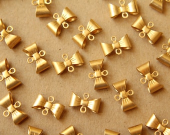 May include: A collection of gold-toned metal bow-shaped clasps with two loops on each clasp. The clasps are scattered on a brown surface.