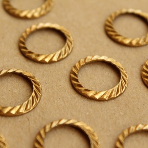 Pode incluir: Um grupo de anéis de metal dourado com um design texturizado e torcido. Os anéis estão dispostos sobre uma superfície marrom.