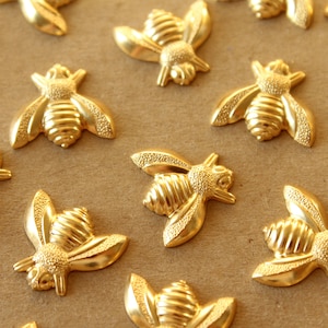 May include: A collection of gold-toned bee-shaped metal embellishments. The bees have detailed wings and bodies with a textured surface.